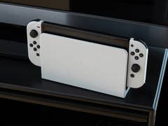 Eine Nintendo Switch OLED-Konsole in Weiß, auf einem schwarzen Regal platziert.