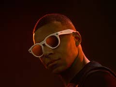 Eine Person mit weißen Sonnenbrillen vor einem dunklen Hintergrund.