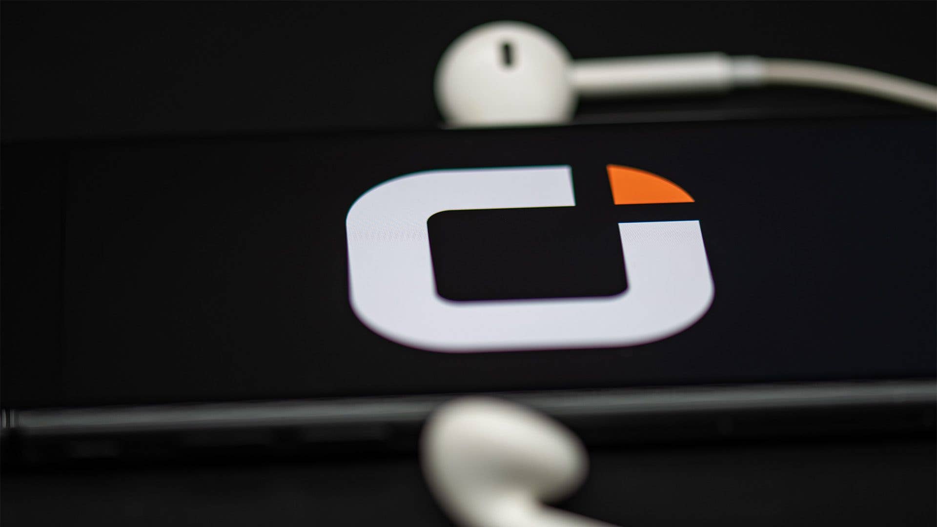 Logo von Otelo auf dem Bildschirm eines Smartphones mit weißen Kopfhörern in der Nähe.