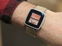 Ein Handgelenk mit einer Pebble Time Smartwatch, die Uhrzeit und Standort anzeigt.