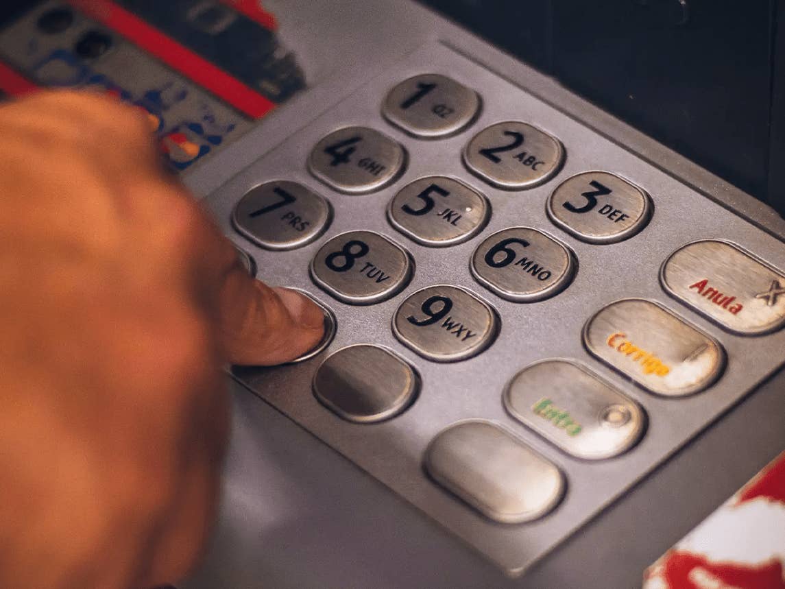 Eine Hand drückt die Nummer 8 auf einer Geldautomaten-Tastatur.