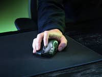 Eine Hand verwendet eine Razer Naga V2 Hyperspeed Gaming-Maus auf einem schwarzen Mauspad.