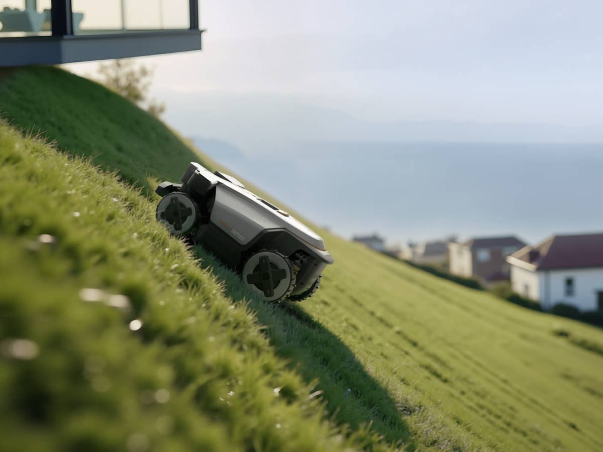 Roborock RockMow Z1 mäht Gras auf einem geneigten Rasen neben einem modernen Haus mit Blick auf das Meer.