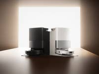 Zwei Roborock-Roboterstaubsauger, einer schwarz und einer weiß, auf einer Holzoberfläche mit einem hellen Hintergrund.