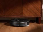 Ein Roborock Qrevo S5V-Roboterstaubsauger auf einem Holzboden unter einem Schrank.