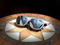 Sonnenbrille auf einem gemusterten Tisch, der die Wolken darüber spiegelt.