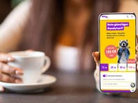 Eine Person hält ein Smartphone, das die Mobilfunktarife von SIMon mobile anzeigt, mit einer Tasse Kaffee im Hintergrund.