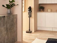 Ein kabelloser Samsung-Staubsauger steht an einer Wand in einem modernen Raum mit hellem Holzfußboden.