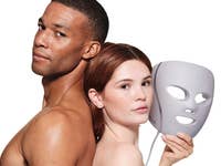 Eine Frau hält eine Shark CryoGlow LED-Maske und steht mit einem shirtlosen Mann Rücken an Rücken.