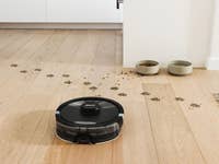 Ein Shark Matrix Plus 2-in-1 Saug- und Wischroboter auf einem Holzboden mit Futtergeschirr im Hintergrund.