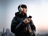 Person trägt SteelSeries Arctis Nova Elite Gaming-Headset und hält ein Smartphone vor einer Stadtsilhouette.