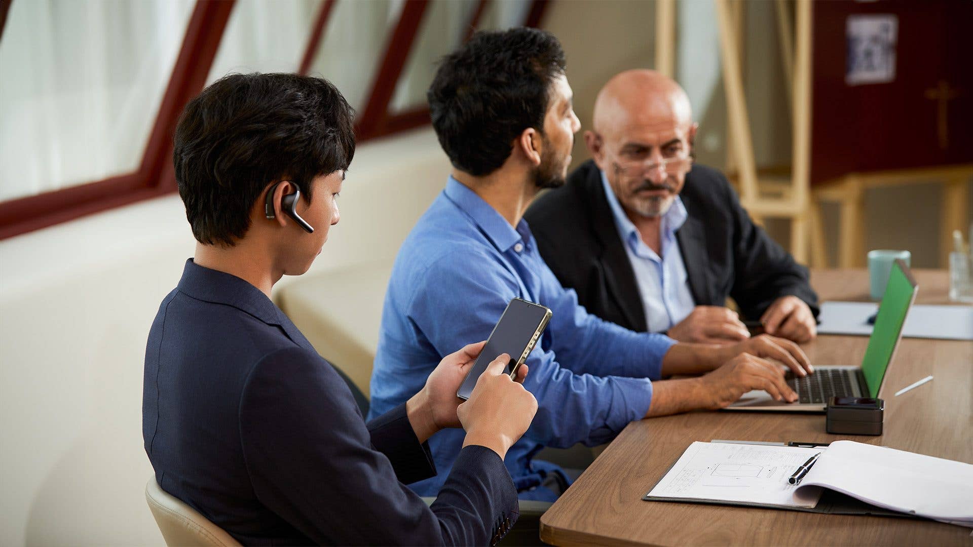 Drei Männer in einer Besprechung, einer am Telefon, nutzen Timekettle W4 Pro zur Kommunikation.