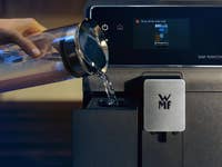Eine Person gießt Wasser in eine WMF-Kaffeemaschine mit einem digitalen Display.