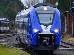 Ein blauer Wasserstoffzug auf Gleisen in Berlin, mit einem Stationsschild im Hintergrund.