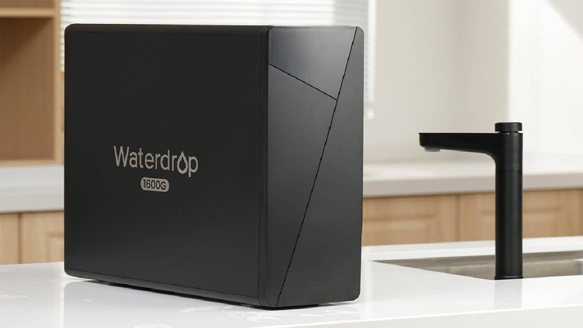 Ein schwarzes Waterdrop-Wasserfiltersystem mit der Bezeichnung 'Waterdrop 1600G' auf einer Küchenarbeitsplatte neben einem Wasserhahn.