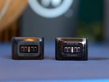 Zwei WHOOP-Geräte auf einem Tisch: eines mit der Bezeichnung 'WHOOP 5.0' und das andere 'WHOOP MG'.