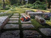 Ein Rasenmäher-Roboter, der auf Steinwegen in einem Landschaftsgarten fährt.