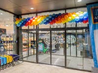 Eingang eines ALDI-Marktes, dekoriert mit bunten Ballons und einem Banner mit der Aufschrift 'Willkommen'.