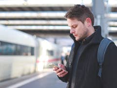 Mann mit Smartphone auf einem Bahnhof