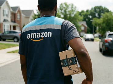 Ein Paketzusteller von Amazon trägt ein kleines Amazon-Päckchen unter dem Arm.