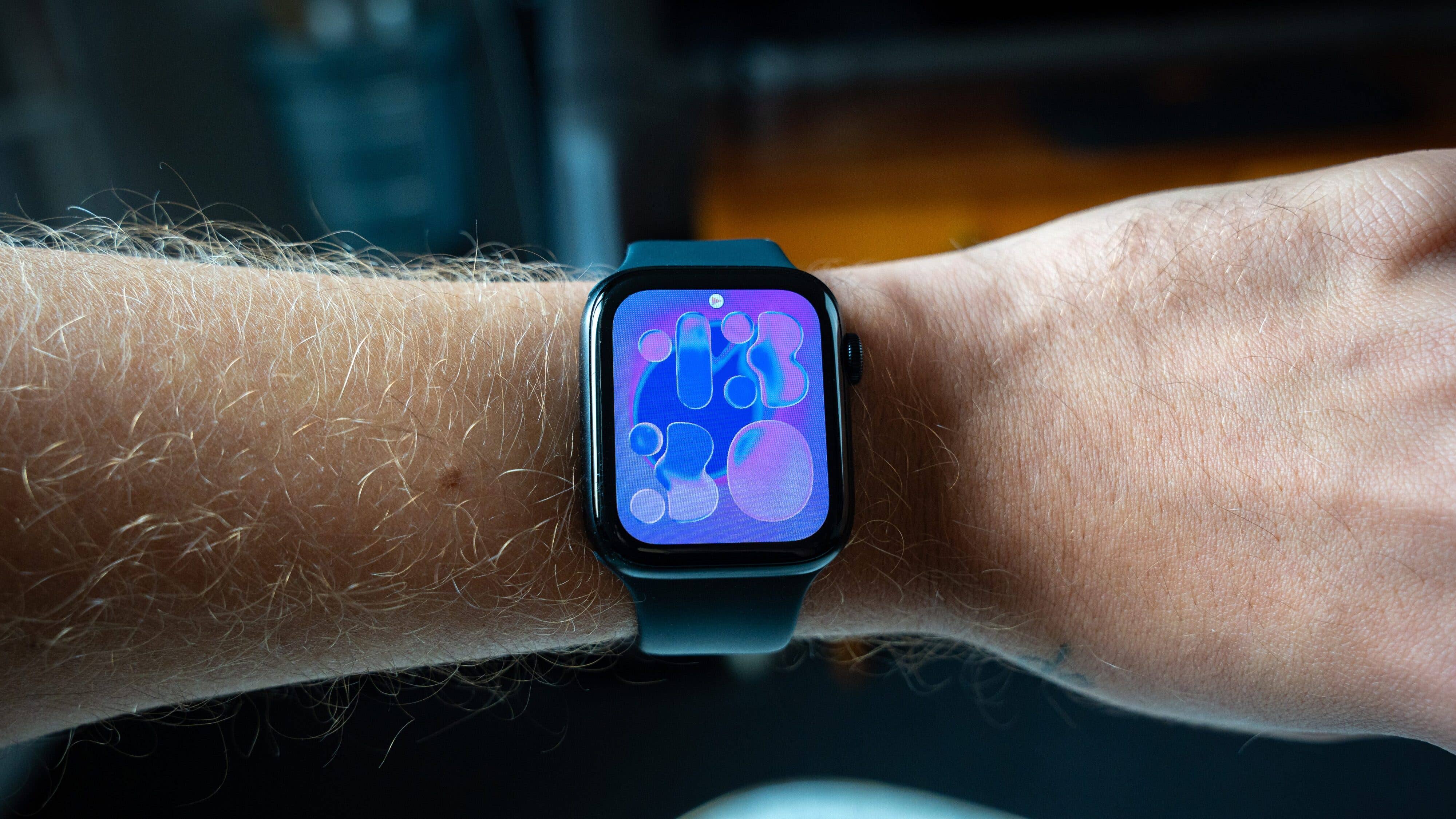 Wie schlägt sich die Apple Watch SE 3 im Test? Nahaufnahme einer Apple Watch SE 3 an einem Handgelenk mit farbigem, abstraktem Zifferblatt.