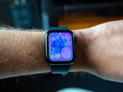 Nahaufnahme einer Apple Watch SE 3 an einem Handgelenk mit farbigem, abstraktem Zifferblatt.