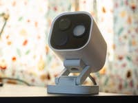 Eine weiße Aqara-Kamerahub G5 Pro auf einer schwarzen Oberfläche mit einem bunten gemusterten Hintergrund.