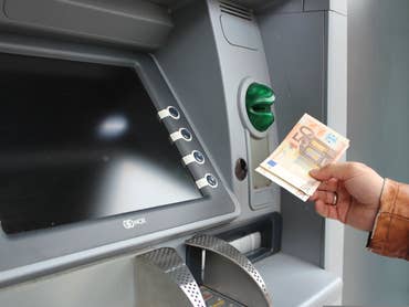 Eine Person, die einen Geldautomaten benutzt, um Bargeld abzuheben, hält einen 50-Euro-Schein.