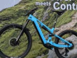 Ein blauer Bosch e-Bike 2025, der auf einem Holzständer vor einem grünen Berghintergrund präsentiert wird.