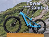 Ein blauer Bosch e-Bike 2025, der auf einem Holzständer vor einem grünen Berghintergrund präsentiert wird.