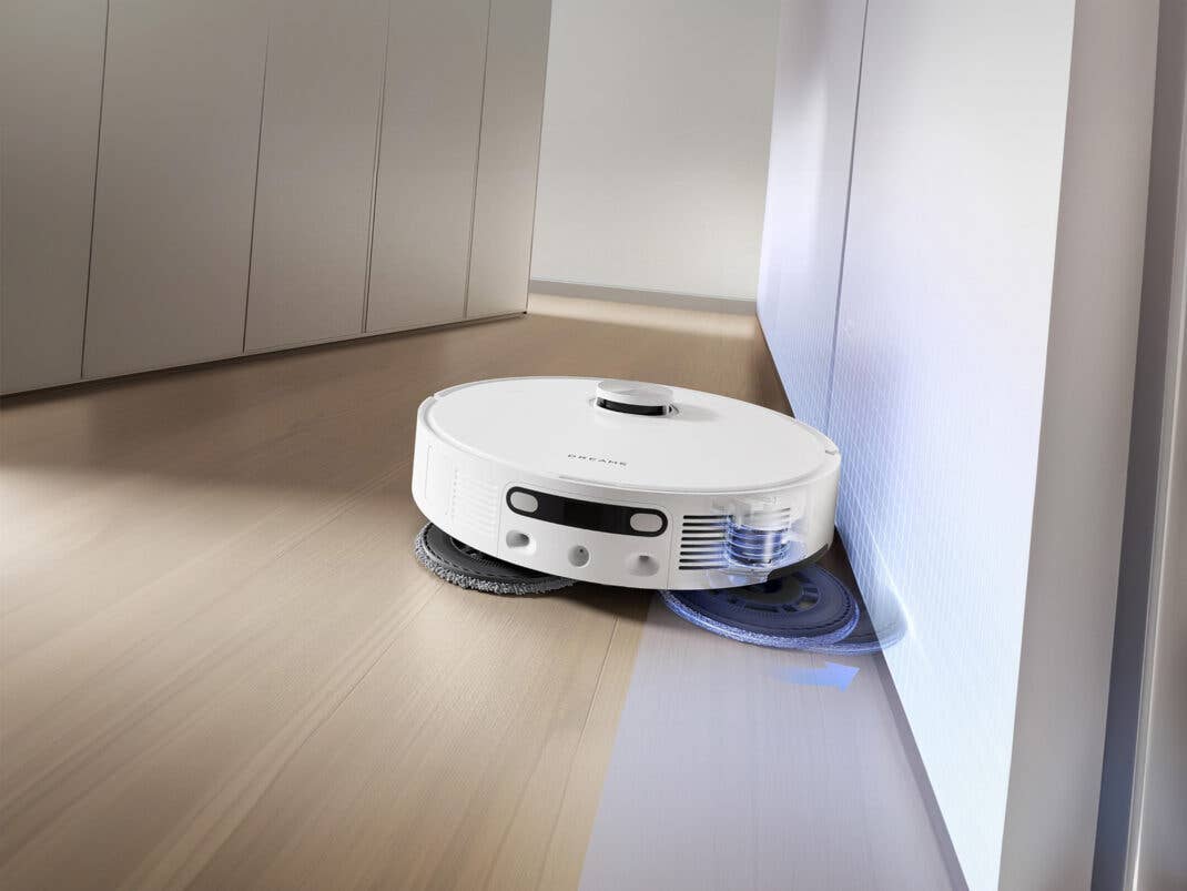 Ein Dreame L10s Ultra Gen 2 Saugroboter reinigt einen Holzfußboden in der Nähe einer Wand. Dreame L10s Ultra Gen2 wischt den Boden