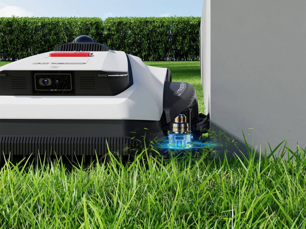 Ein Mähroboter bearbeitet eine Rasenfläche an einer Hauswand