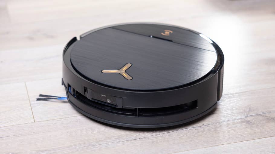 Ein schlanker schwarzer Staubsaugerroboter auf einem Holzboden.
