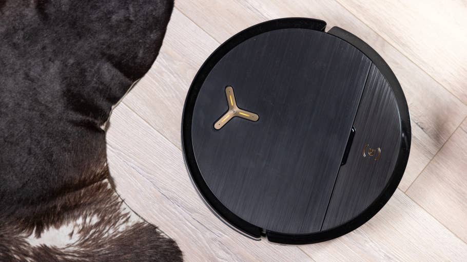 Ein schwarzer Ecovacs Deebot X9 Pro Omni Staubsauger auf Holzboden neben einem braunen Pelzteppich.
