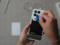 Eine Person verwendet ein Werkzeug, um die Rückseite eines Fairphone 6-Smartphones zu öffnen und die Batterie sichtbar zu machen.