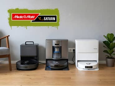 Drei Saug- und Wischroboter, die in einem Zimmer auf dem Boden stehen, MediaMarkt/Saturn-Logo darüber auf grünem Hintergrund.