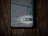 Google Maps-App zeigt ein Tempolimit von 20 km/h und eine Geschwindigkeit von 0 km/h auf einer Holzoberfläche.