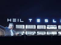 Eine Projektion einer Person mit dem Text 'HEIL TESLA' auf einem Gebäude bei Nacht.