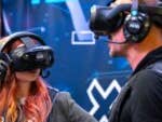 Zwei Personen mit VR-Headsets erleben eine virtuelle Realität vor einem digitalen Hintergrund.