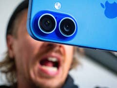 Nahaufnahme einer blauen Apple iPhone 16 Kamera mit einer Person, die im Hintergrund schreit.