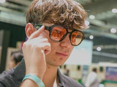 Ein junger Mann trägt stylische Sonnenbrillen und berührt seine Schläfe in einem Innenraum.