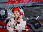 Frau hält eine MediaMarkt-Karte im MediaMarkt-Store. Drumherum Logitech-Geräte