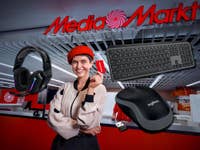 Frau hält eine MediaMarkt-Karte im MediaMarkt-Store. Drumherum Logitech-Geräte