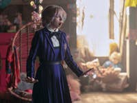 Ein überraschter Mädchen in einem gestreiften Outfit steht in einem bunten Zimmer voller Spielzeug und Dekorationen.