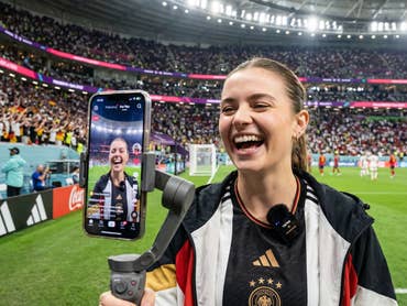 Eine Content Creatorin steht am Spielfeldrand in einem Stadion und spricht in die Handy-Kamera.