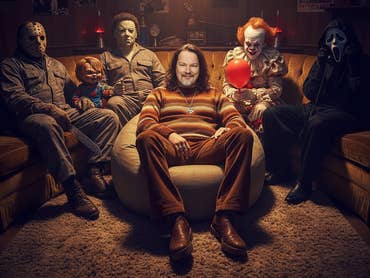 Casi sitzt in einem Sessel, dahinter auf der Couch zahlreiche Horror-Legenden.