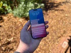 Eine Person hält ein Smartphone, das eine digitale Assistentenoberfläche mit Uhrzeit und Abfragen anzeigt.