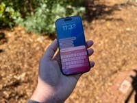 Eine Person hält ein Smartphone, das eine digitale Assistentenoberfläche mit Uhrzeit und Abfragen anzeigt.