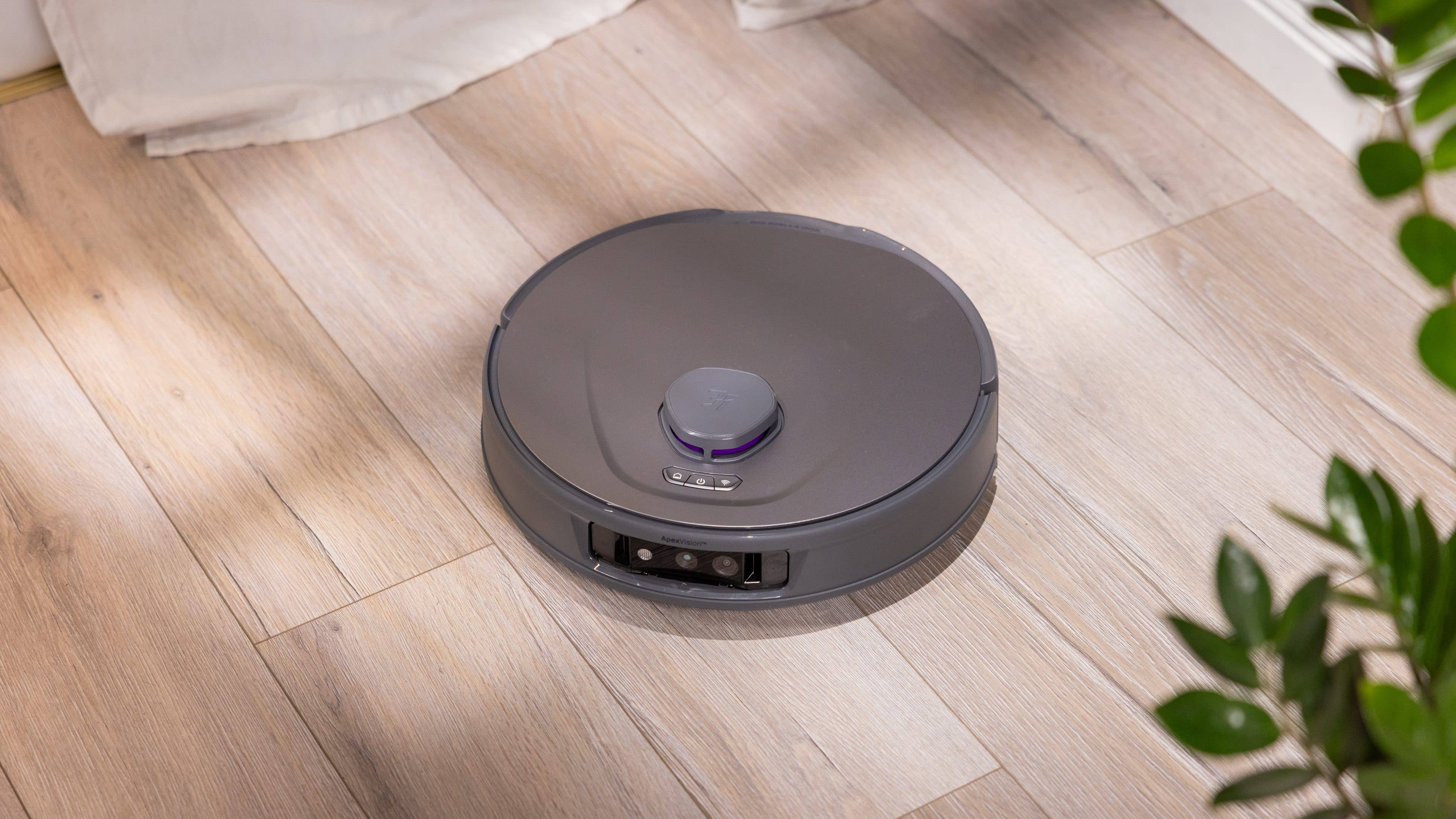 Ein Roboterstaubsauger auf Holzfußboden, mit minimalistischer Gestaltung und einem kleinen Bedienfeld oben.