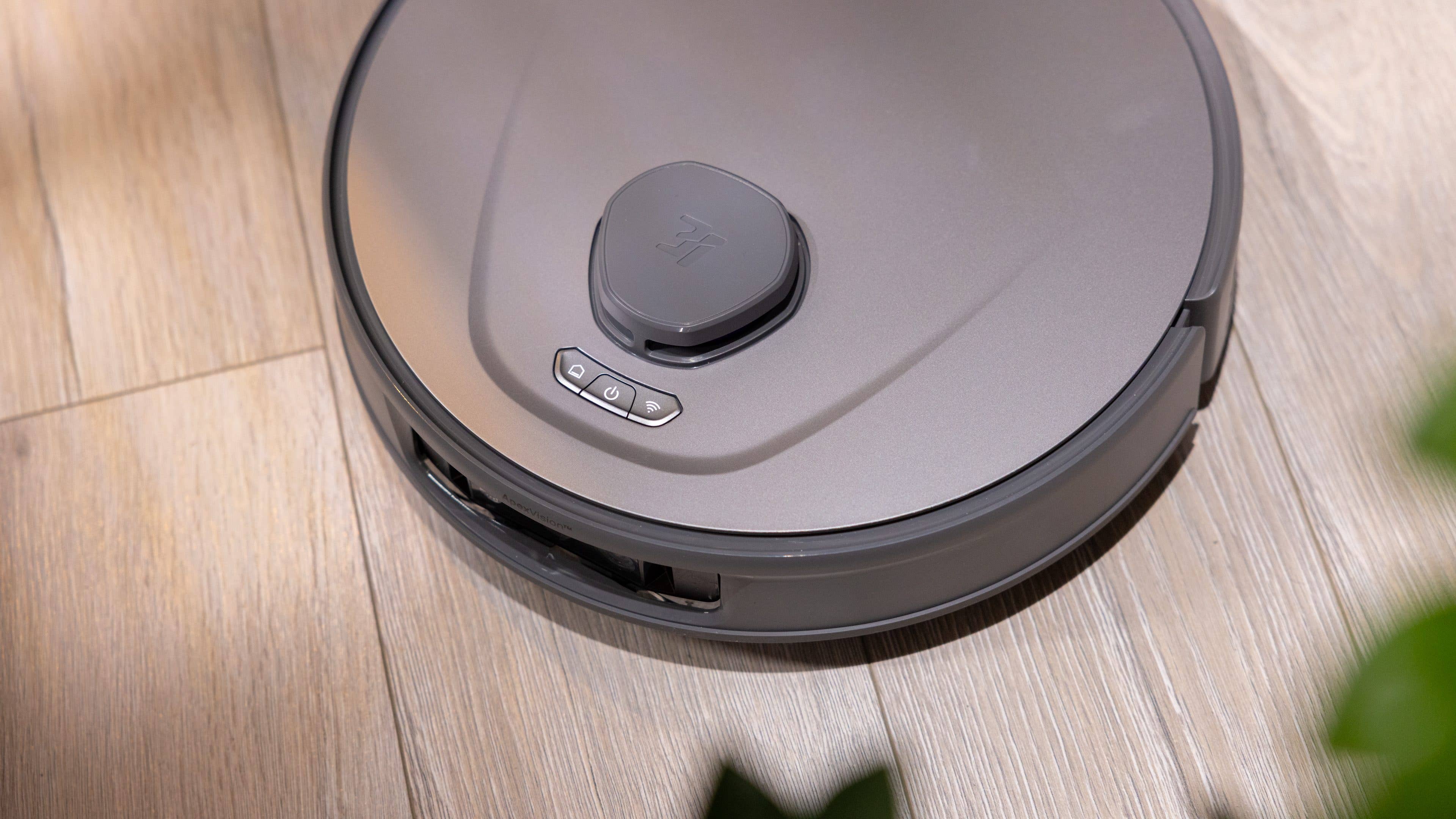 Ein grauer Saugroboter auf holzfarbenem Boden.